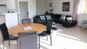 Ein modernes Wohnzimmer mit einer schwarzen Ledersofa, einem Holzespeisetisch mit Stühlen und einer Küche im Hintergrund.