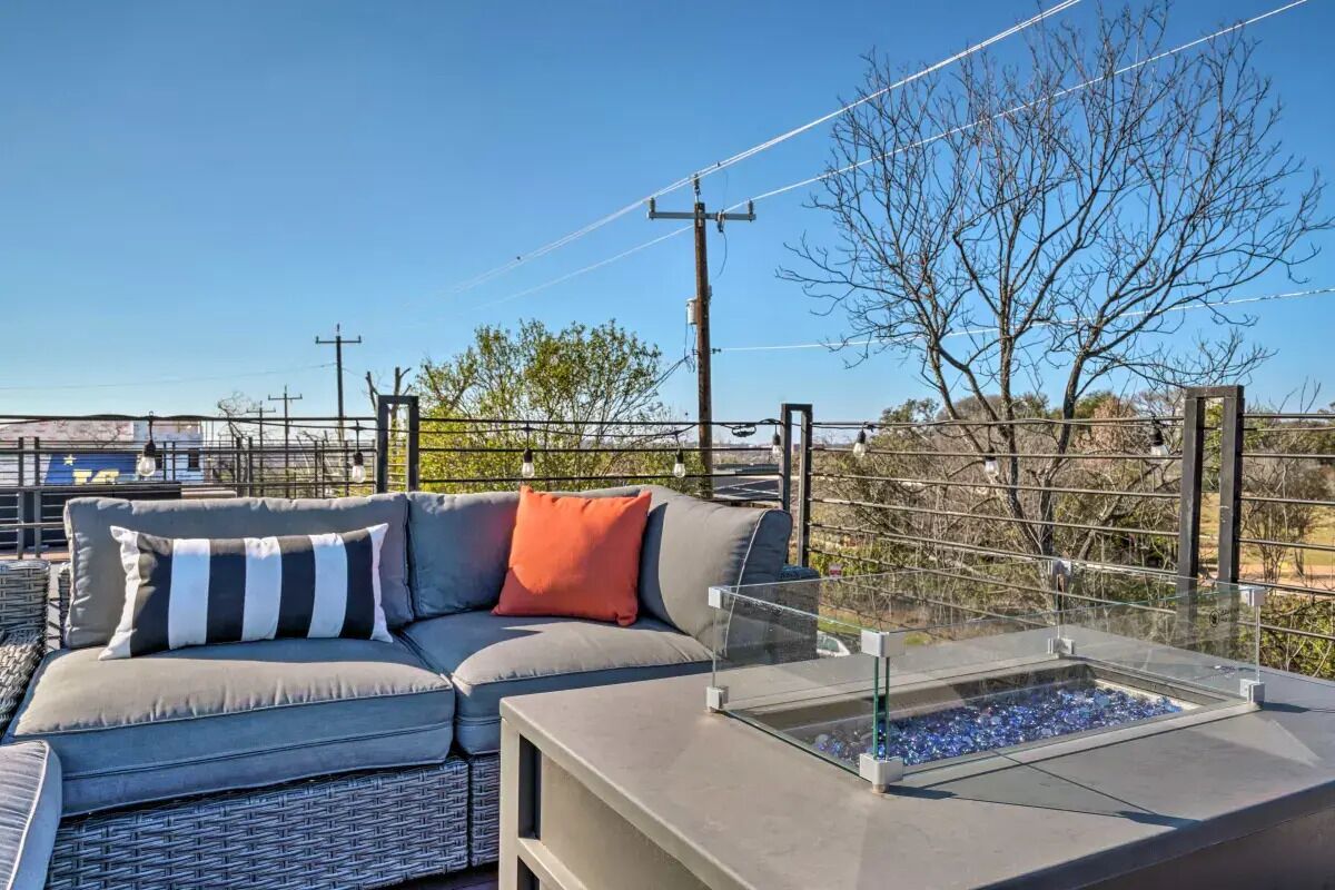 A modern outdoor seating area with a gray sofa and a glass table, overlooking a landscape with trees and power lines.