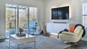 Moderni olohuone, jossa on lasiovi, joka johtaa parvekkeelle, seinälle asennettu taulutelevisio ja mukava sohva.