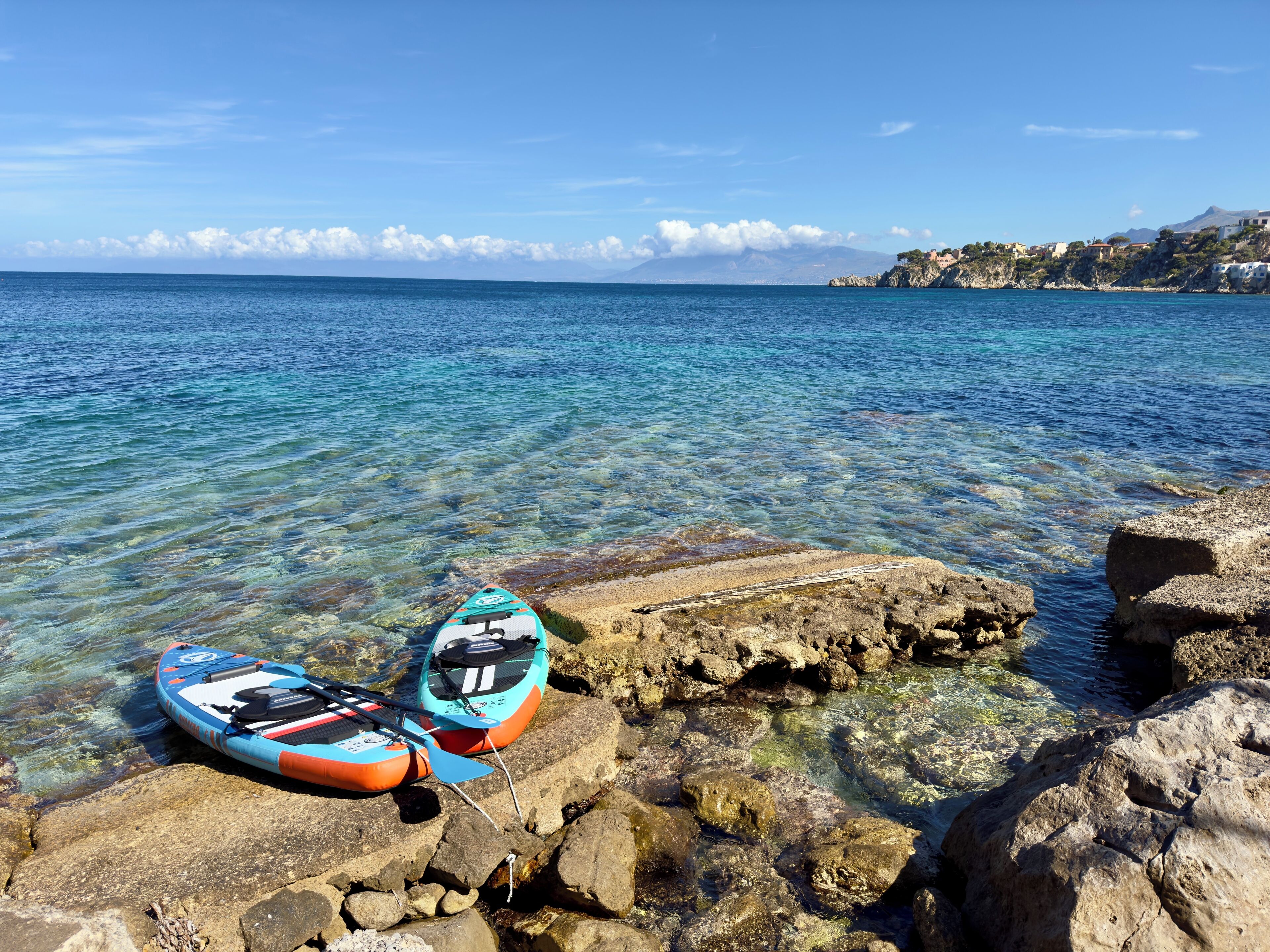 Two kayaks on rocky shore with clear water and a mountainous backdrop.