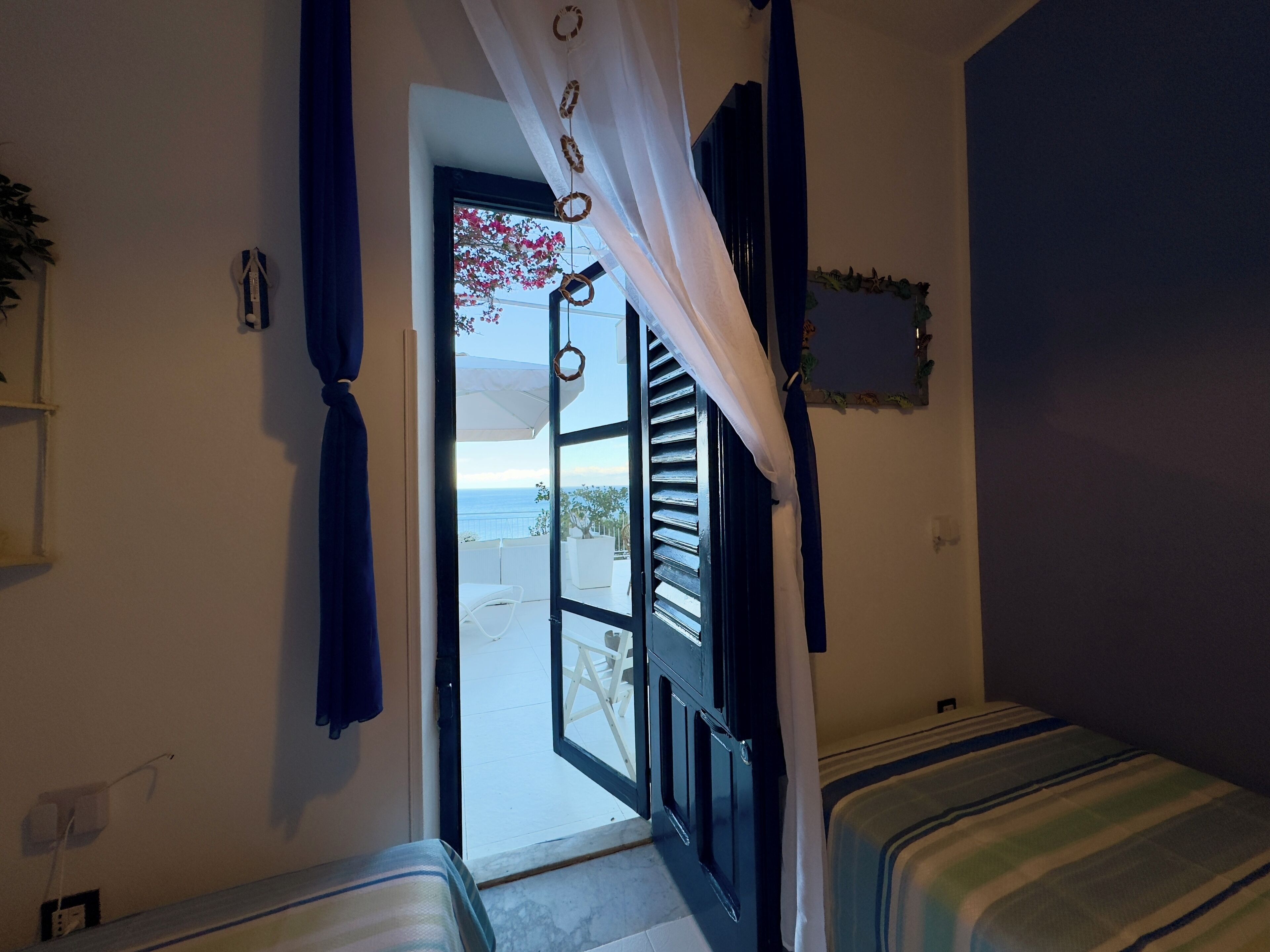 A room with a bed, a window with curtains, and a view of the sea.