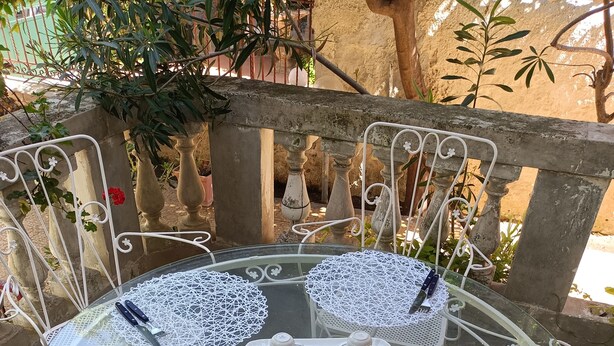 A round glass table with white metal chairs, a white lace tablecloth, and a tray with teacups and a sugar bowl. - 1 Bedroom Apartment in Mondello (Mondello)