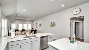 A spacious kitchen with white cabinetry, a dishwasher, and a large island with a sink. There is a clock on the wall and a door leading to another room. - Exquisite 4 Bedroom Brand New Home in Katy (Katy)