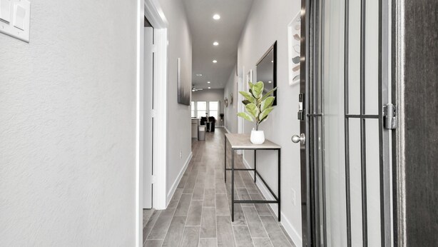A hallway with a tiled floor, a potted plant on a table, and a door with a metal handle. - Exquisite 4 Bedroom Brand New Home in Katy (Katy)