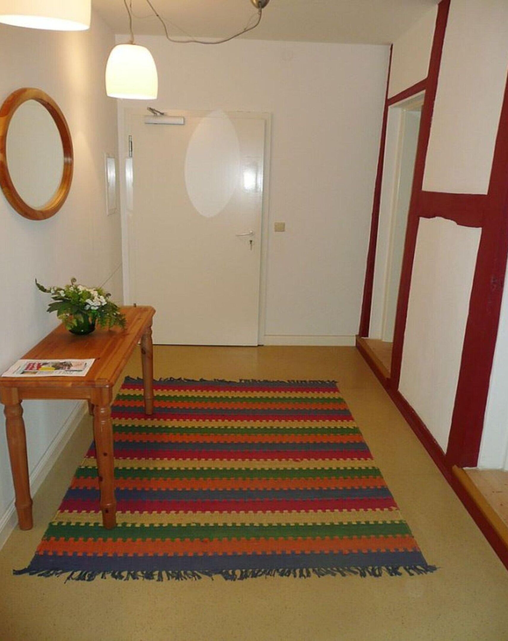 Un pasillo con un banco de madera, un tapiz a rayas de colores, un espejo y una puerta.