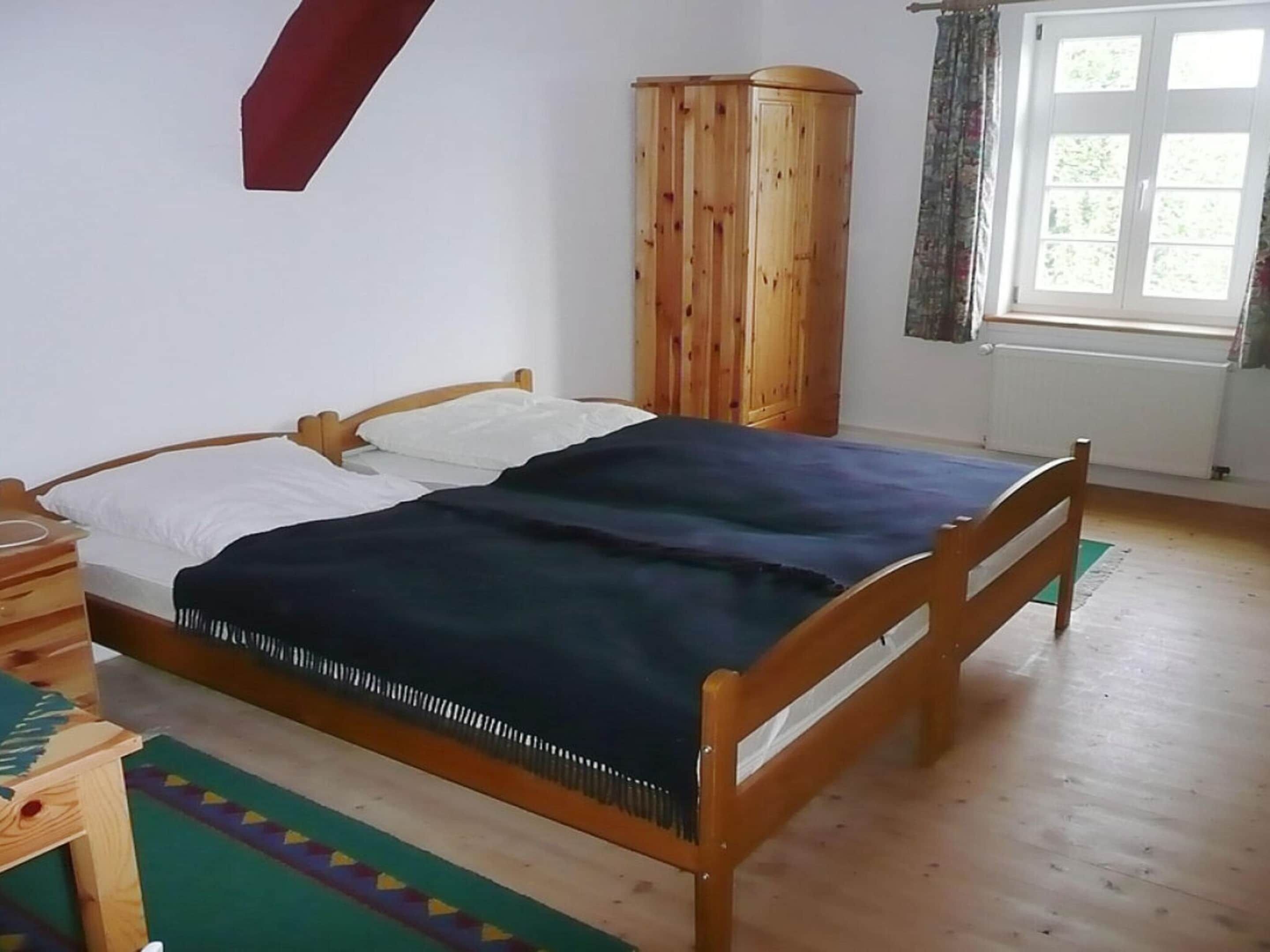 Una cama de madera con colcha azul en una habitación que tiene un armario de madera y un ventanal con cortinas.