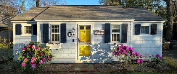 Une petite maison de plain-pied avec une porte jaune, des volets noirs et une façade en briques.