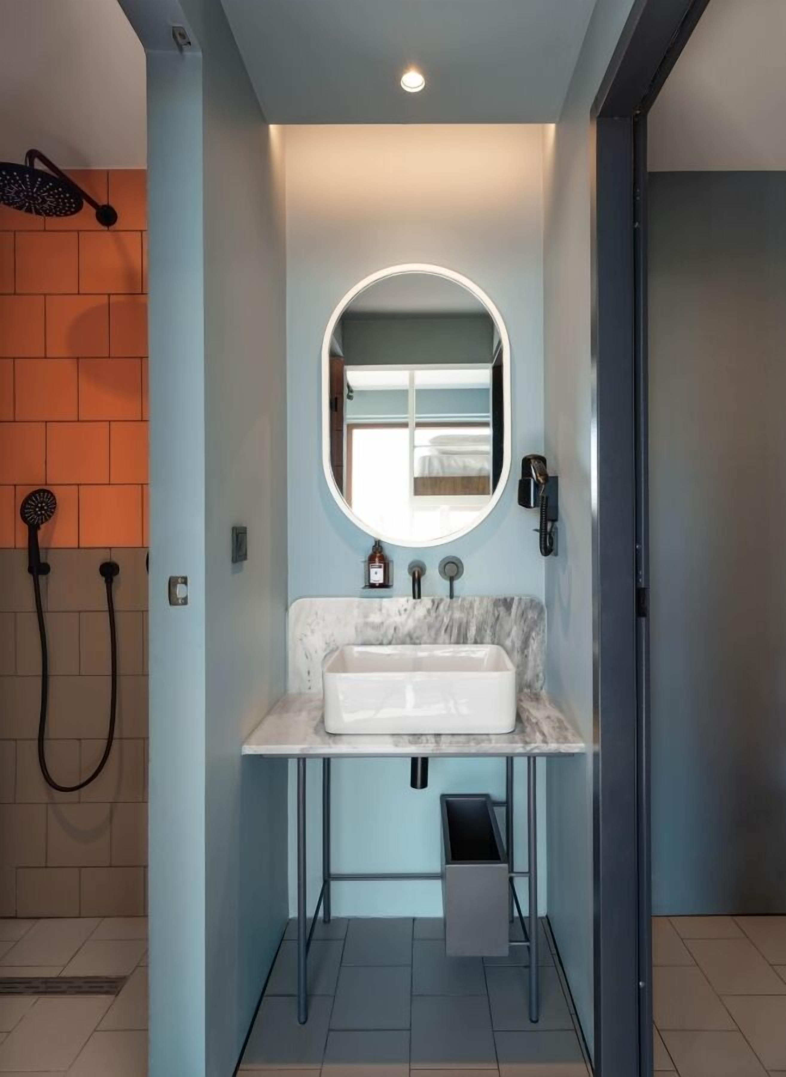 Un baño moderno con lavamanos de mármol, un espejo redondo y un cabezal de ducha.