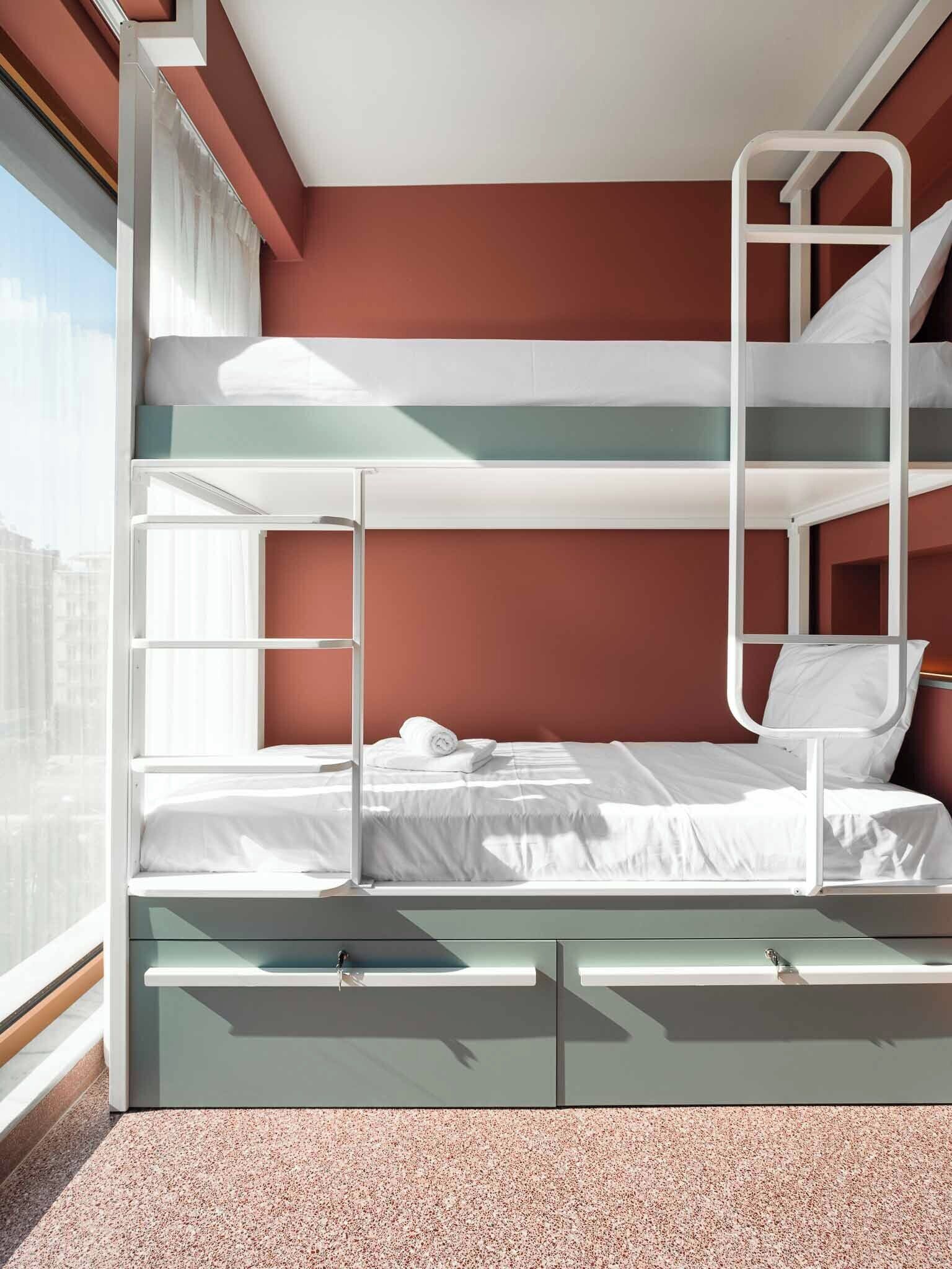 Una cama litera con escalera, una ventana con cortinas y vistas a la ciudad.