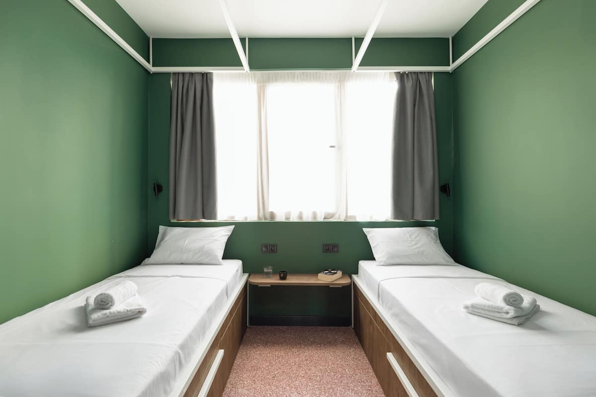 A twin room with two beds, a small table, and a window with curtains.
