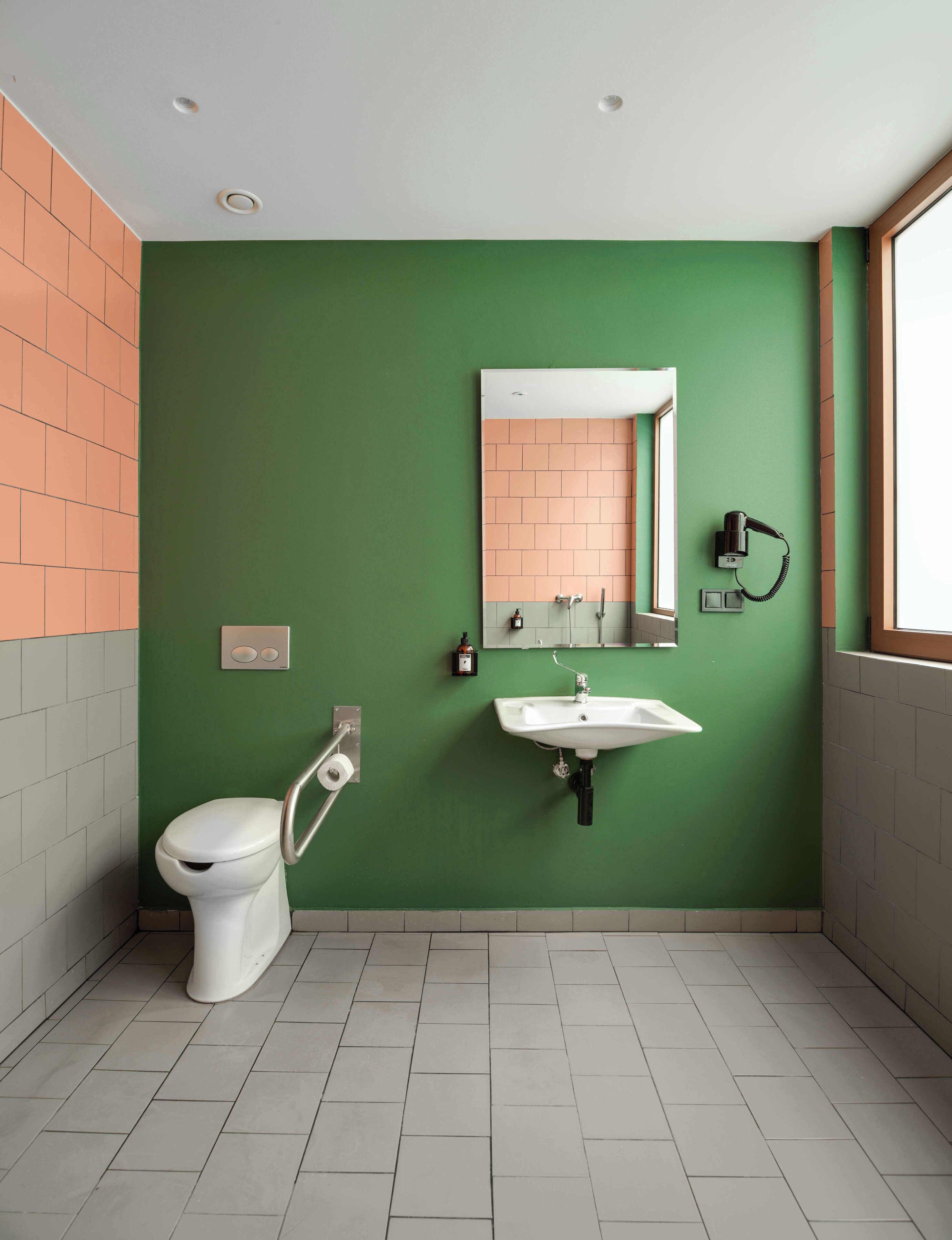 Une salle de bain avec un mur vert, un lavabo blanc, des toilettes et une fenêtre.