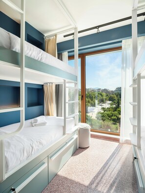 A room with bunk beds, a window with a city view, and a small trash bin. - Zeus is Loose Hostel (Thessaloniki)