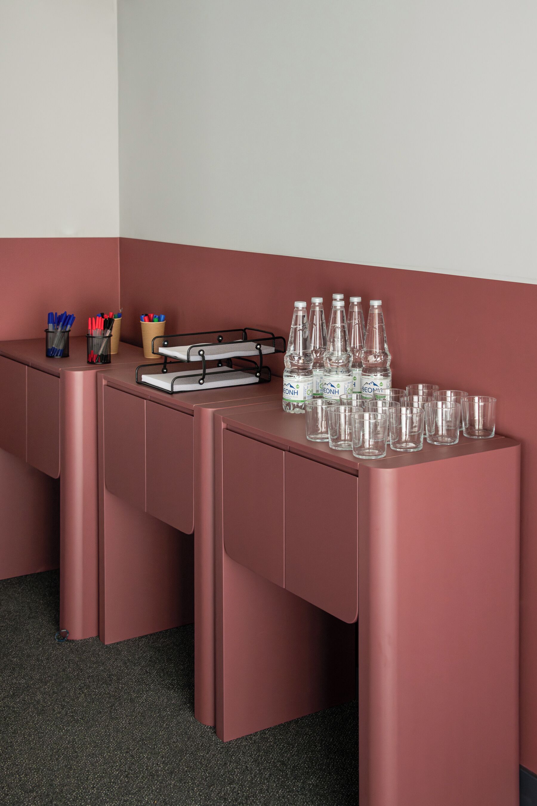 Un mostrador de recepción rosa con bolígrafos, rotuladores y botellas de agua.