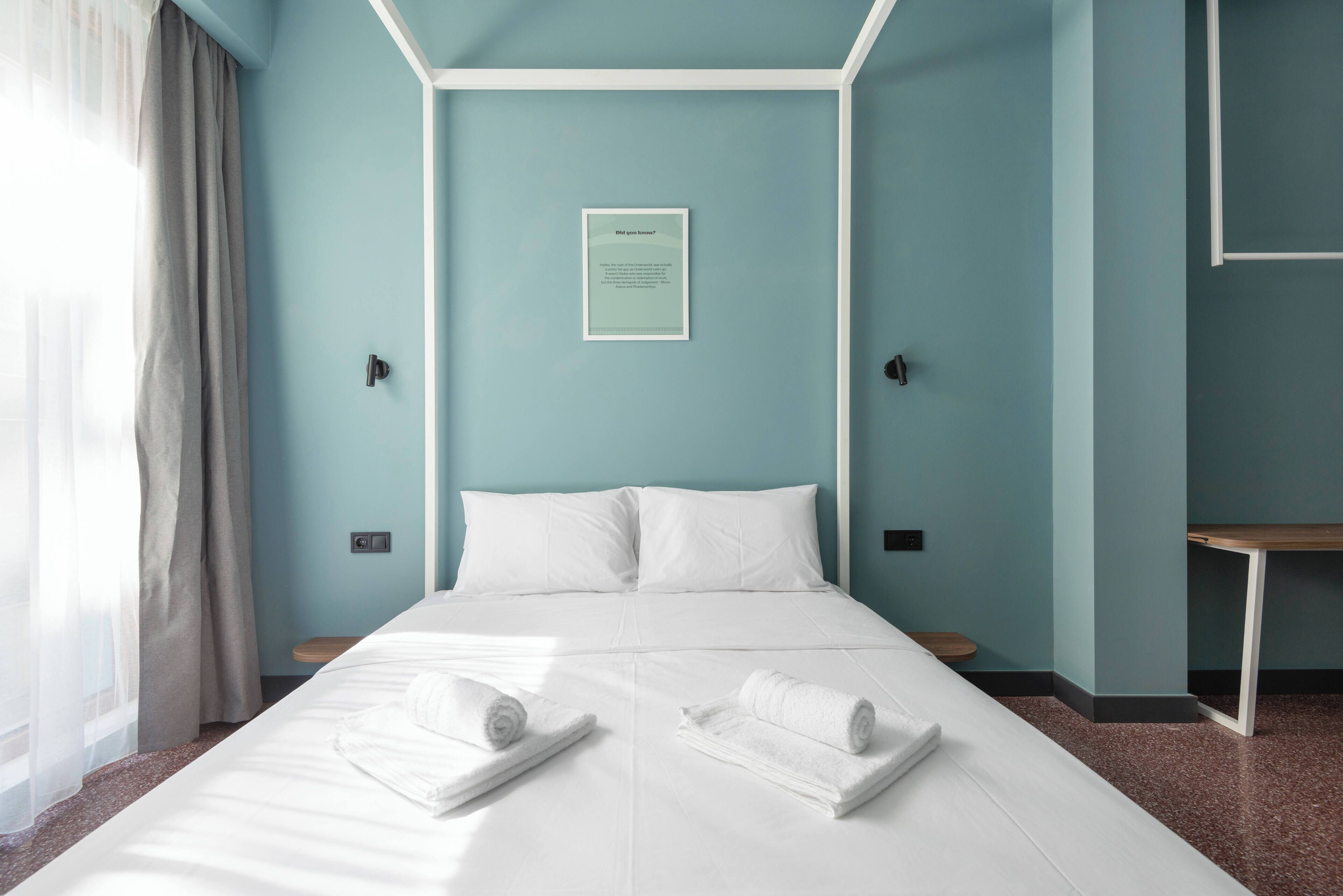 A neatly made bed with white linens and two rolled towels, a framed sign on the wall, and a small table beside the bed.