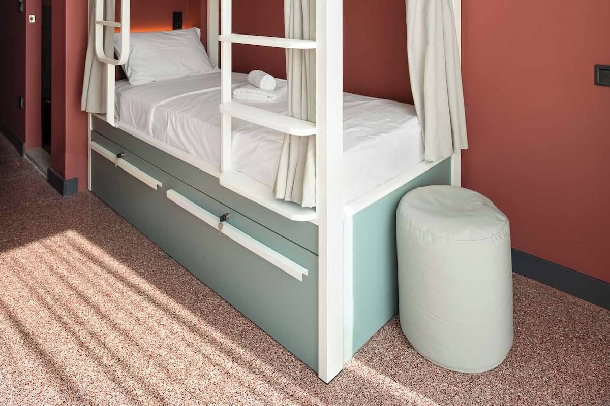 A bunk bed with a pull-out desk and storage drawers, set against a red wall with a white curtain.