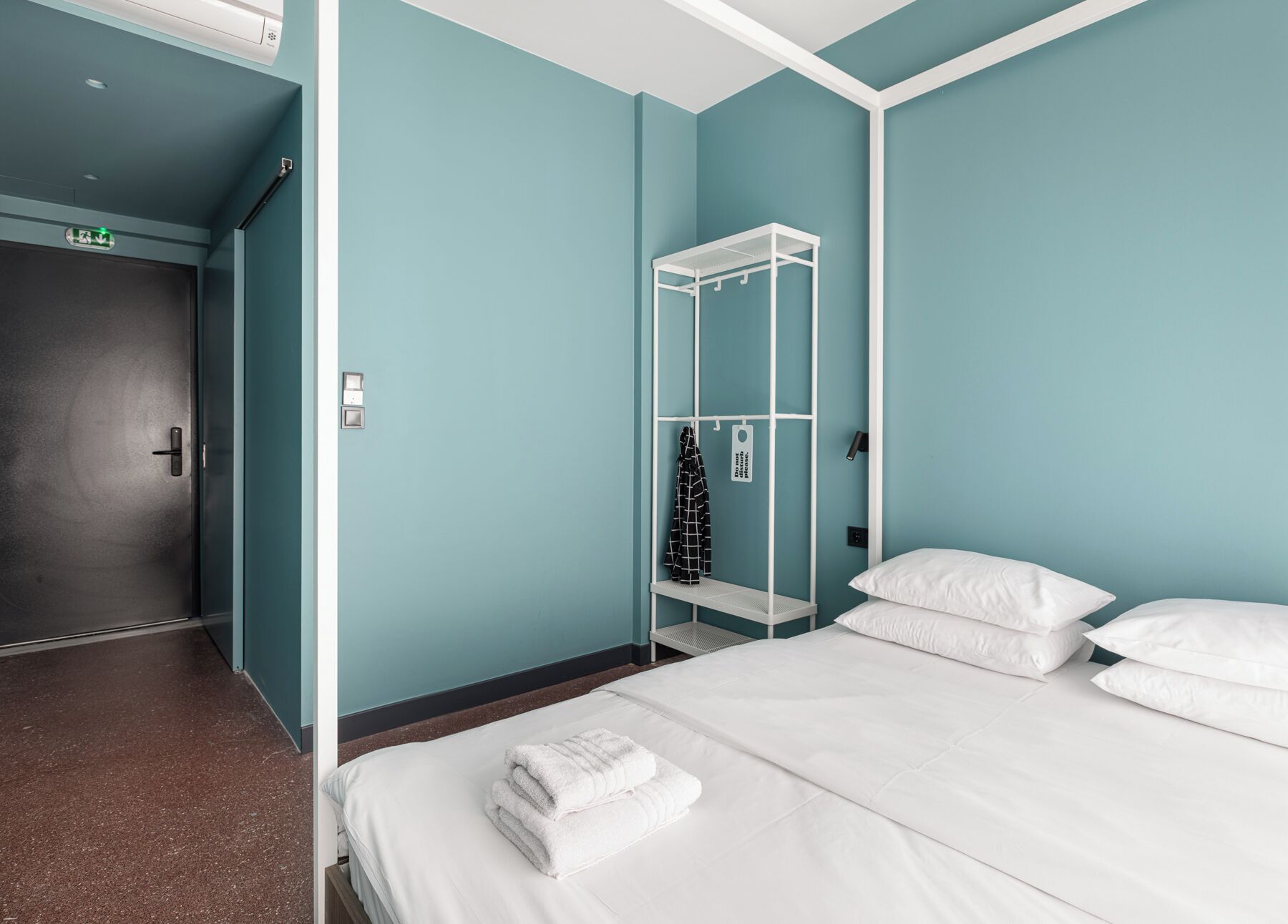 Een hotelkamer met turquoise wanden, een wit bed en een witte inbouwkast.