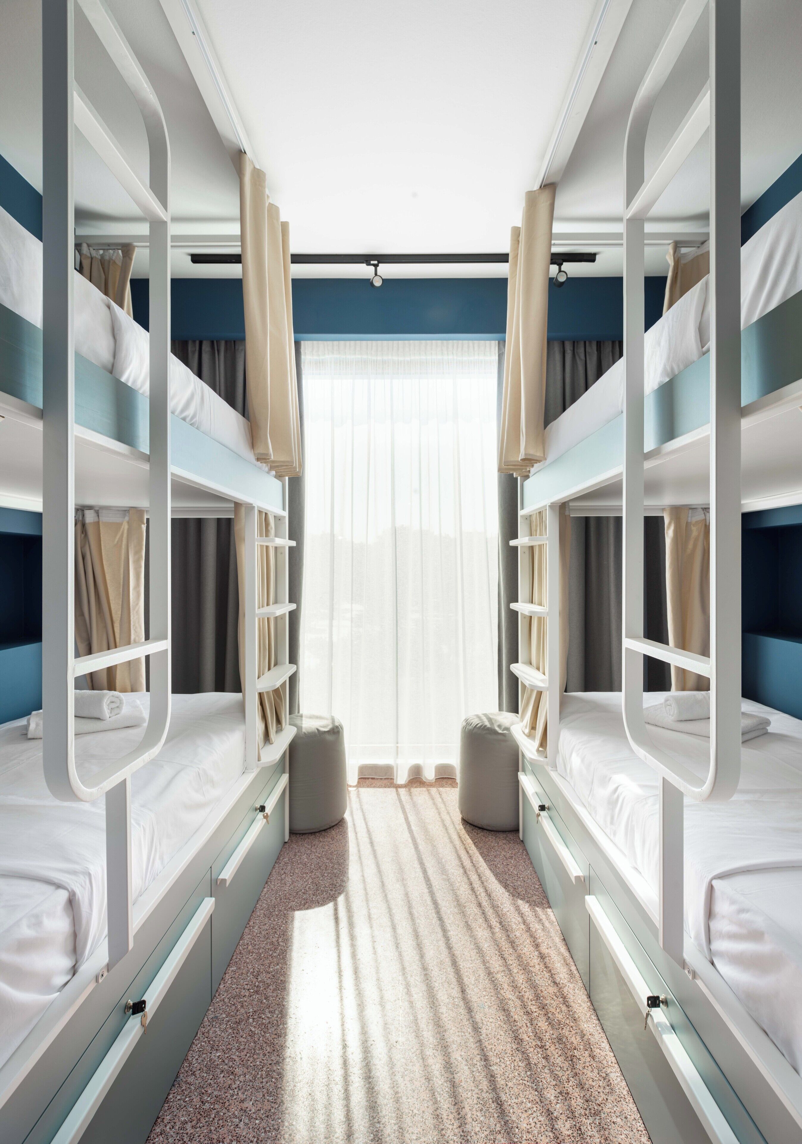 Ein Hotelzimmer mit Etagenbetten, einem fensterbelaubten Fenster, Teppichboden und einer kleinen Sitzecke.
