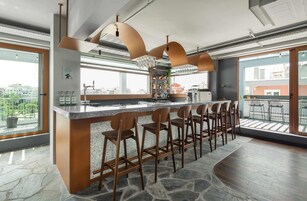 A modern bar area with a central island, bar stools, and a view of the city through large windows.