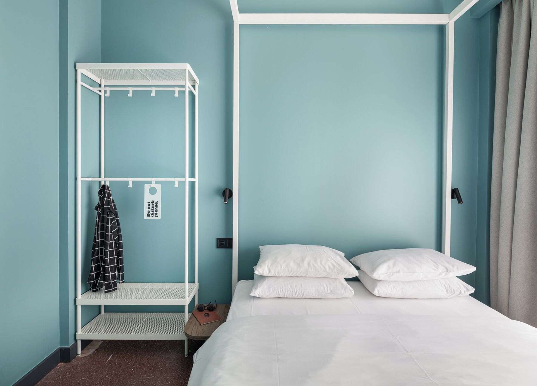 A room with a bed, a white metal wardrobe, and a sign that says "Do not disturb please."