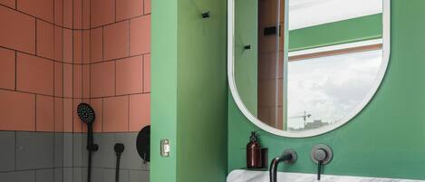 A bathroom with a white sink, green walls, a shower with a black handheld showerhead, and a mirror with a round frame.