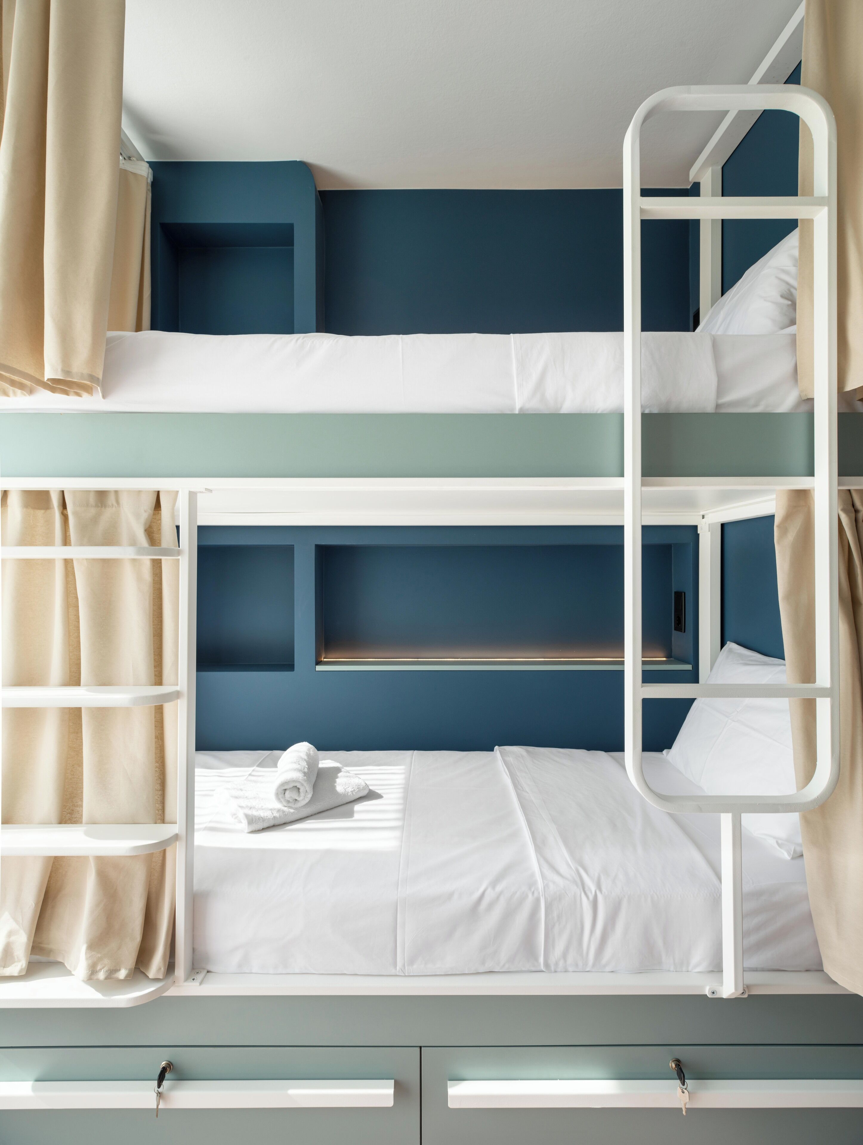 Una cama litera con escalera, un estante pequeño y una ventana con cortinas.