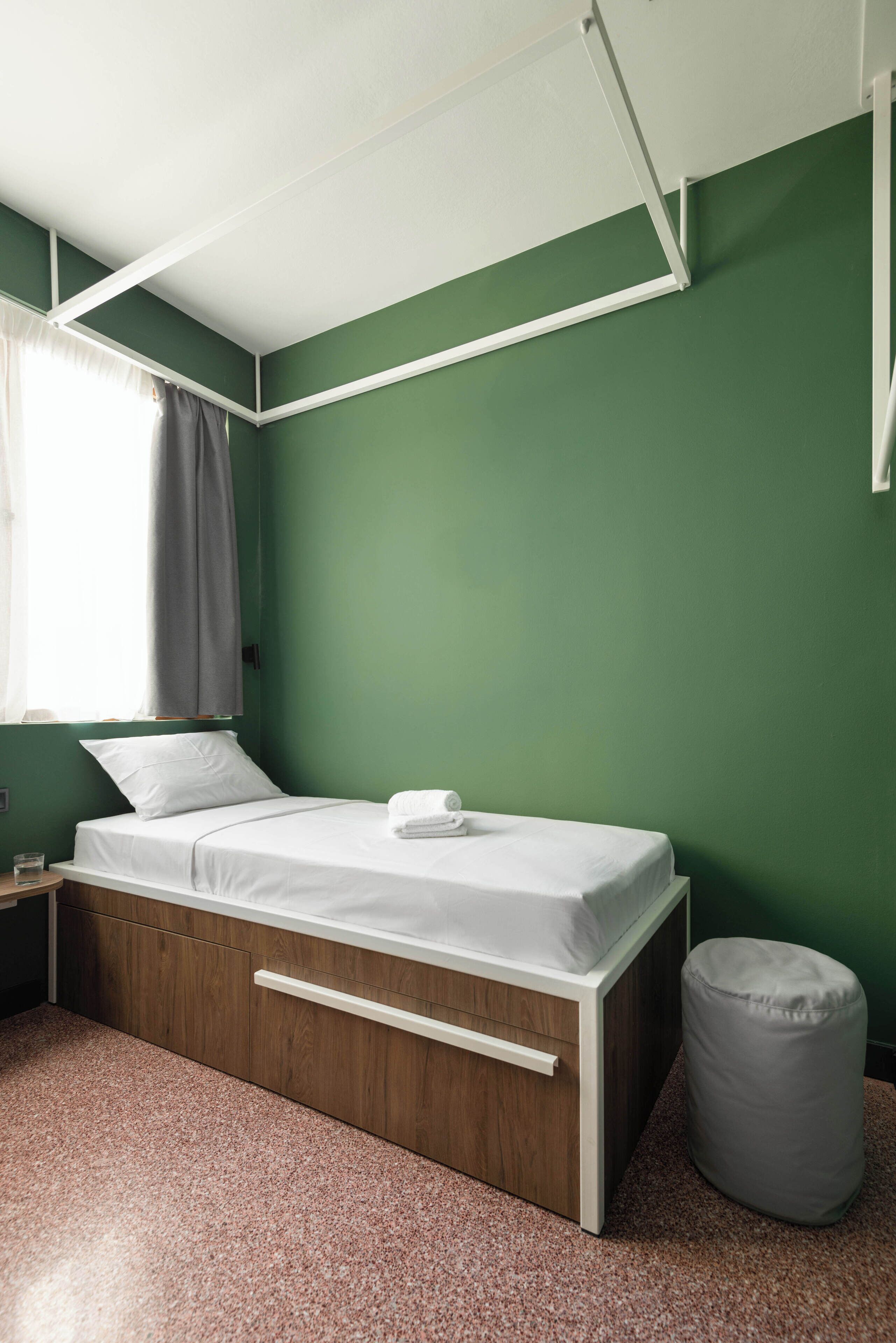 A single-bed room with a wooden frame, a white mattress, and a grey bean bag.