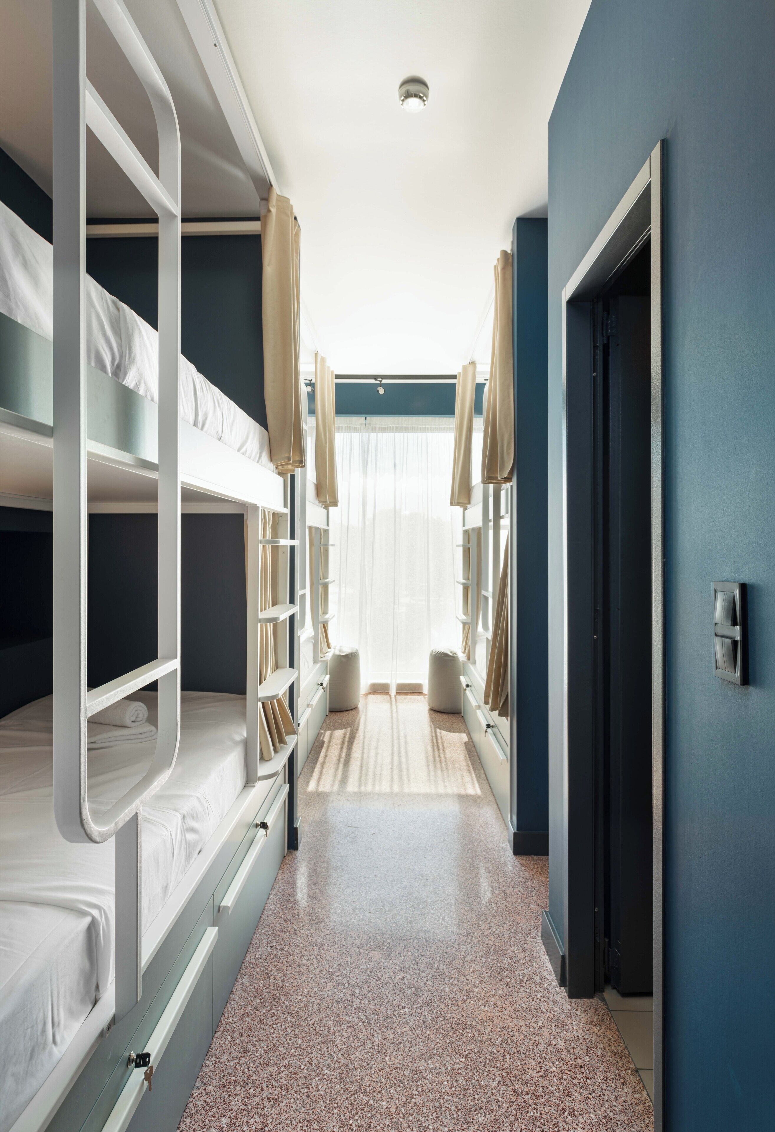 A hotel room with bunk beds, a door, and a window with curtains.