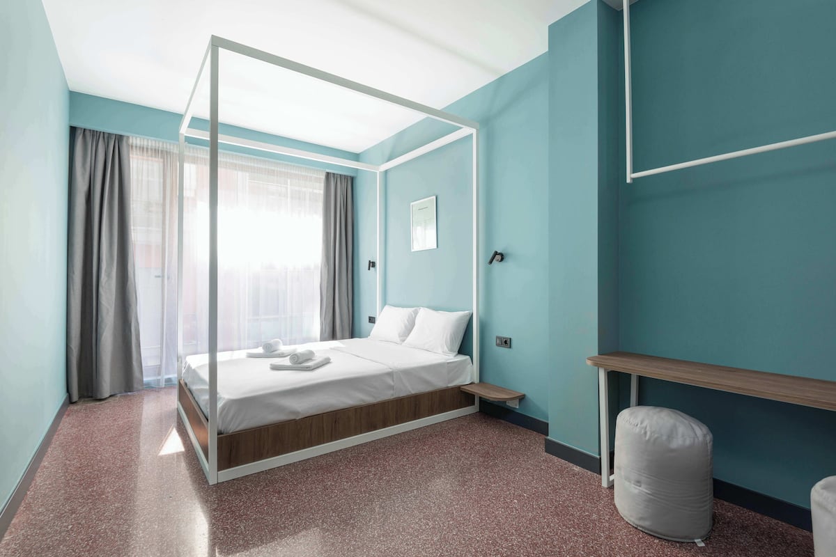 A modern bedroom with a four-poster bed, a wooden nightstand, a small seating area, and a white bean bag.
