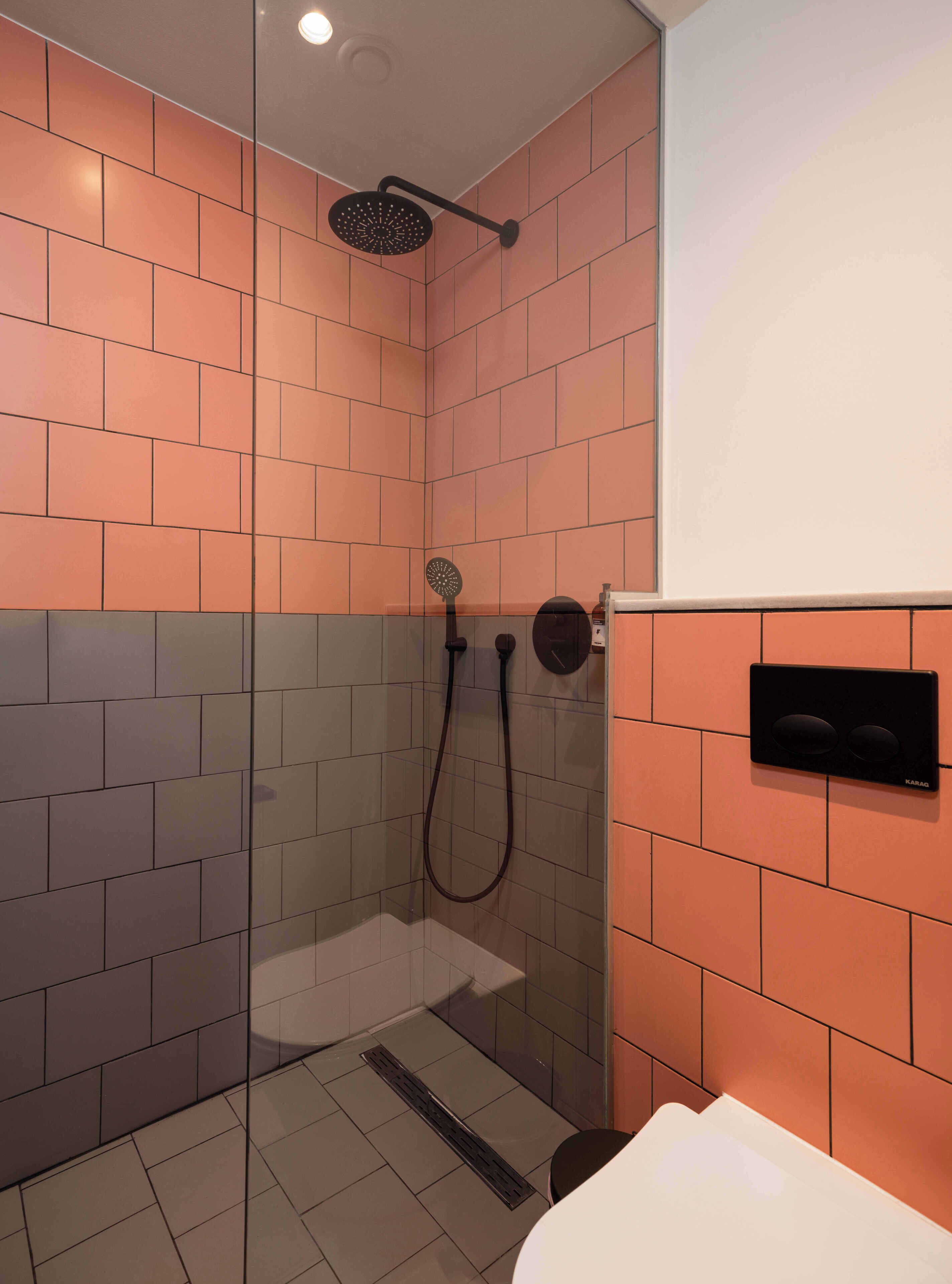 A modern bathroom with orange and gray tiles, a glass shower enclosure, a handheld showerhead, a wall-mounted control panel, and a white sink.