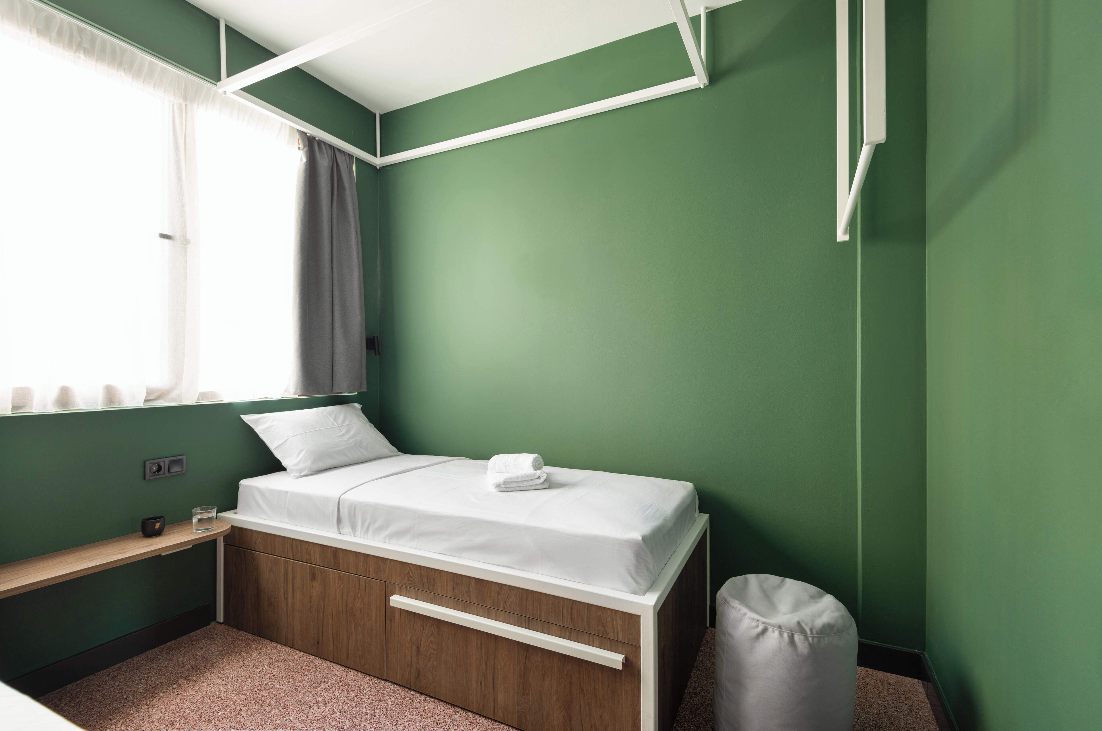 Un dormitorio ordenado con cama, mesita de noche y una ventana pequeña con cortinas.