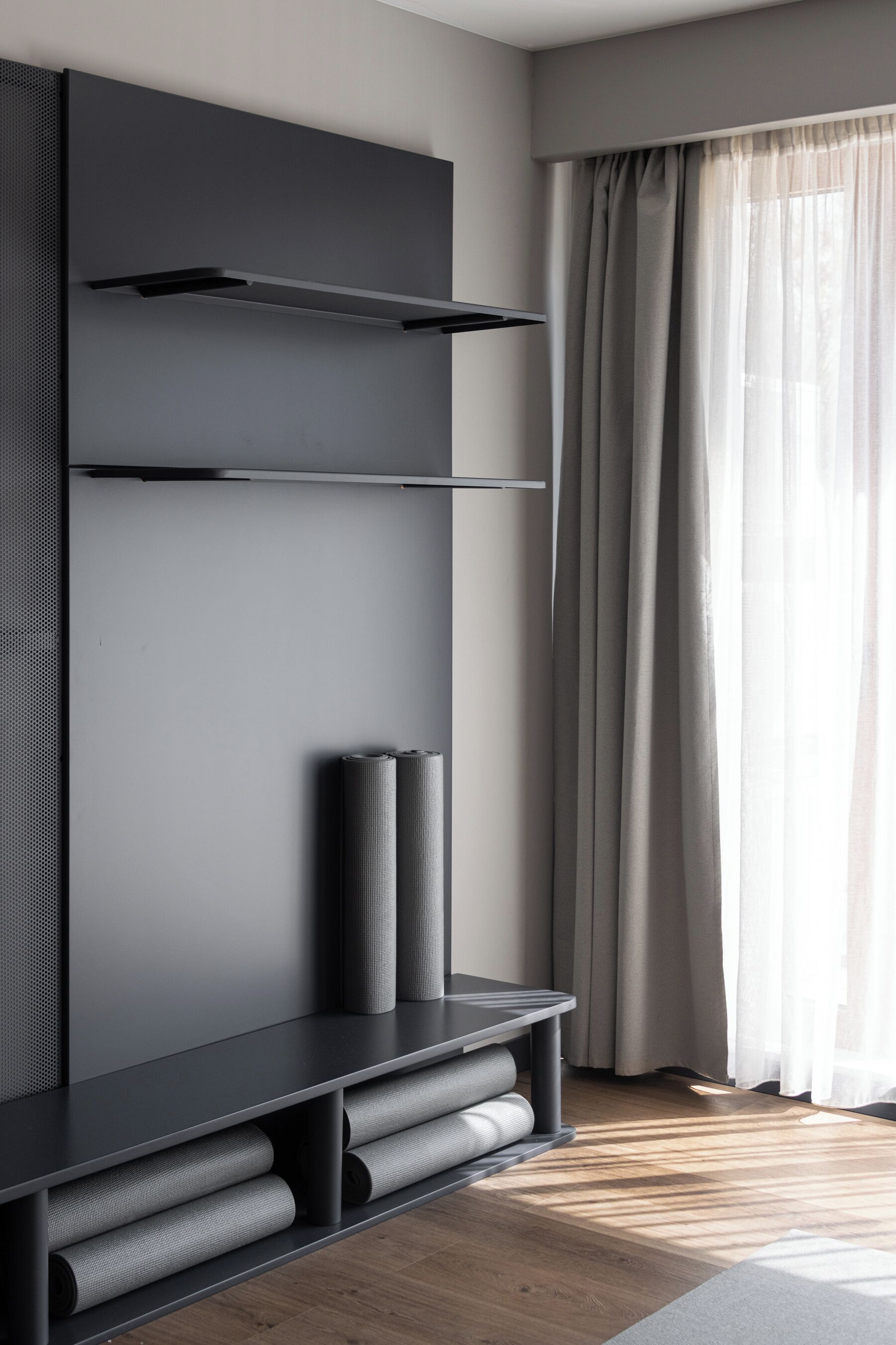 A modern living room with a built-in entertainment unit, a large window with sheer curtains, and a wooden floor.