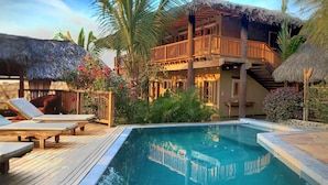 A poolside area with lounge chairs and a thatched-roof building. - VILLA DEL SOL  (Máncora)