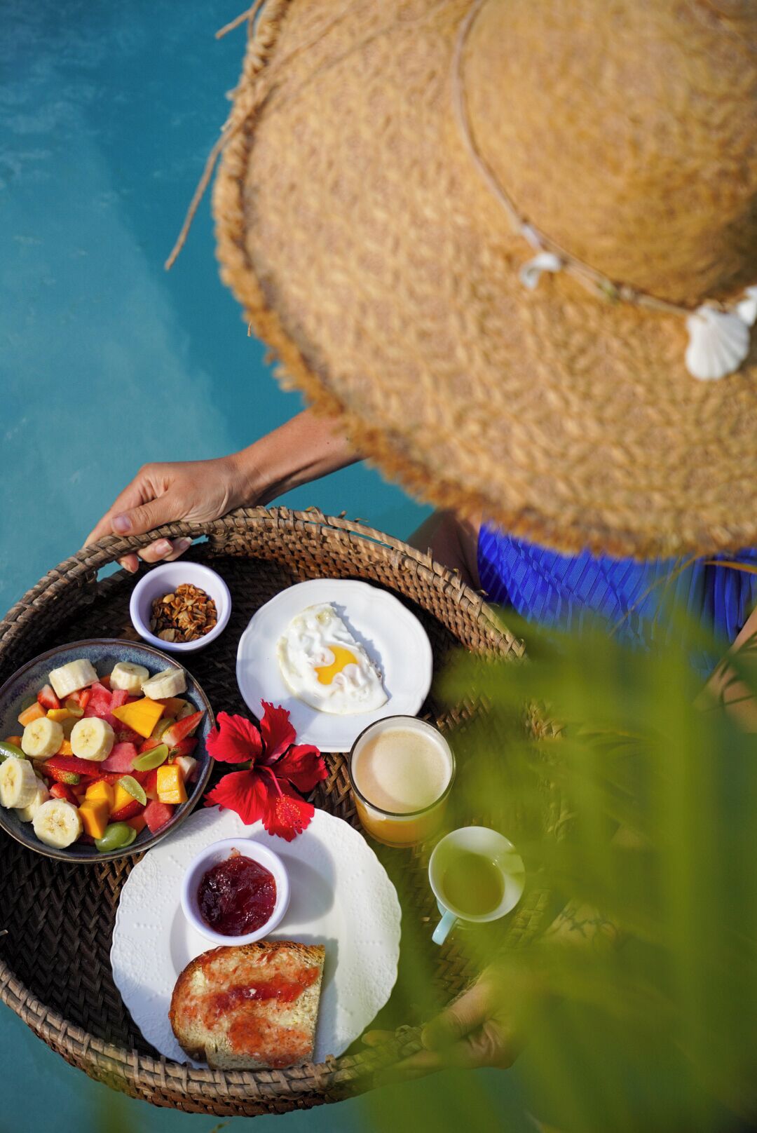 A person holding a wicker tray with breakfast items including fruit, eggs, bread, and beverages.