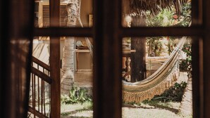 A view through a window with a wooden frame, displaying a hammock, a thatched roof structure, and a garden area with plants and a pathway. - VILLA DEL SOL  (Máncora)