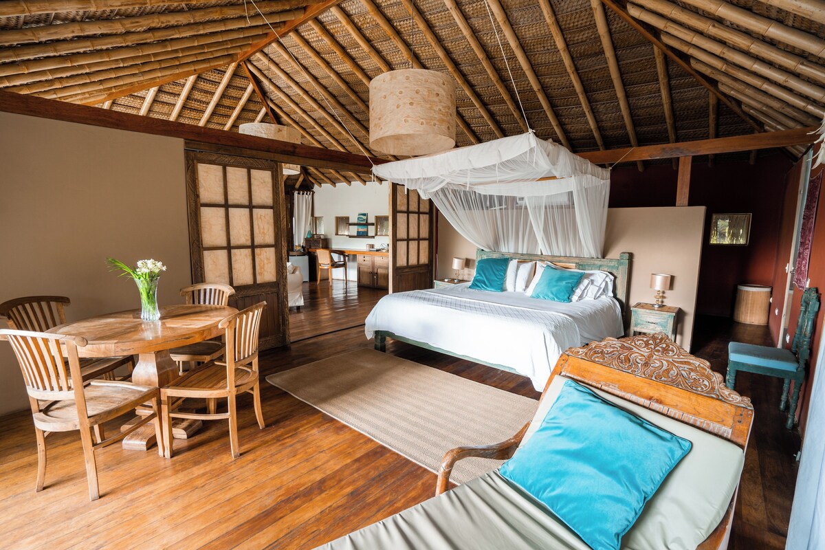 A room with a bed, a dining table with chairs, and a wooden floor.
