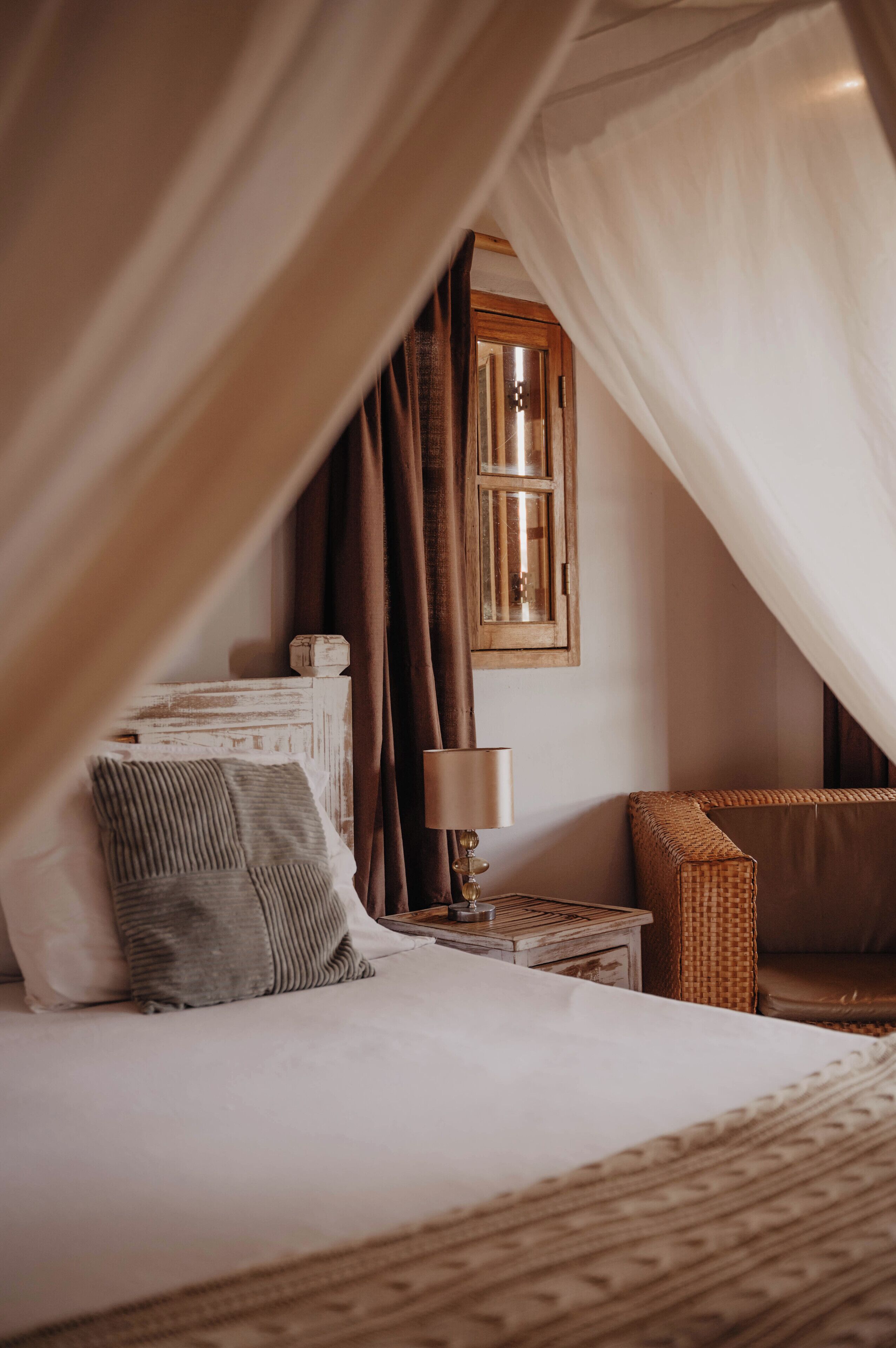 A bedroom with a canopy bed, a bedside table with a lamp, and a wicker chair.