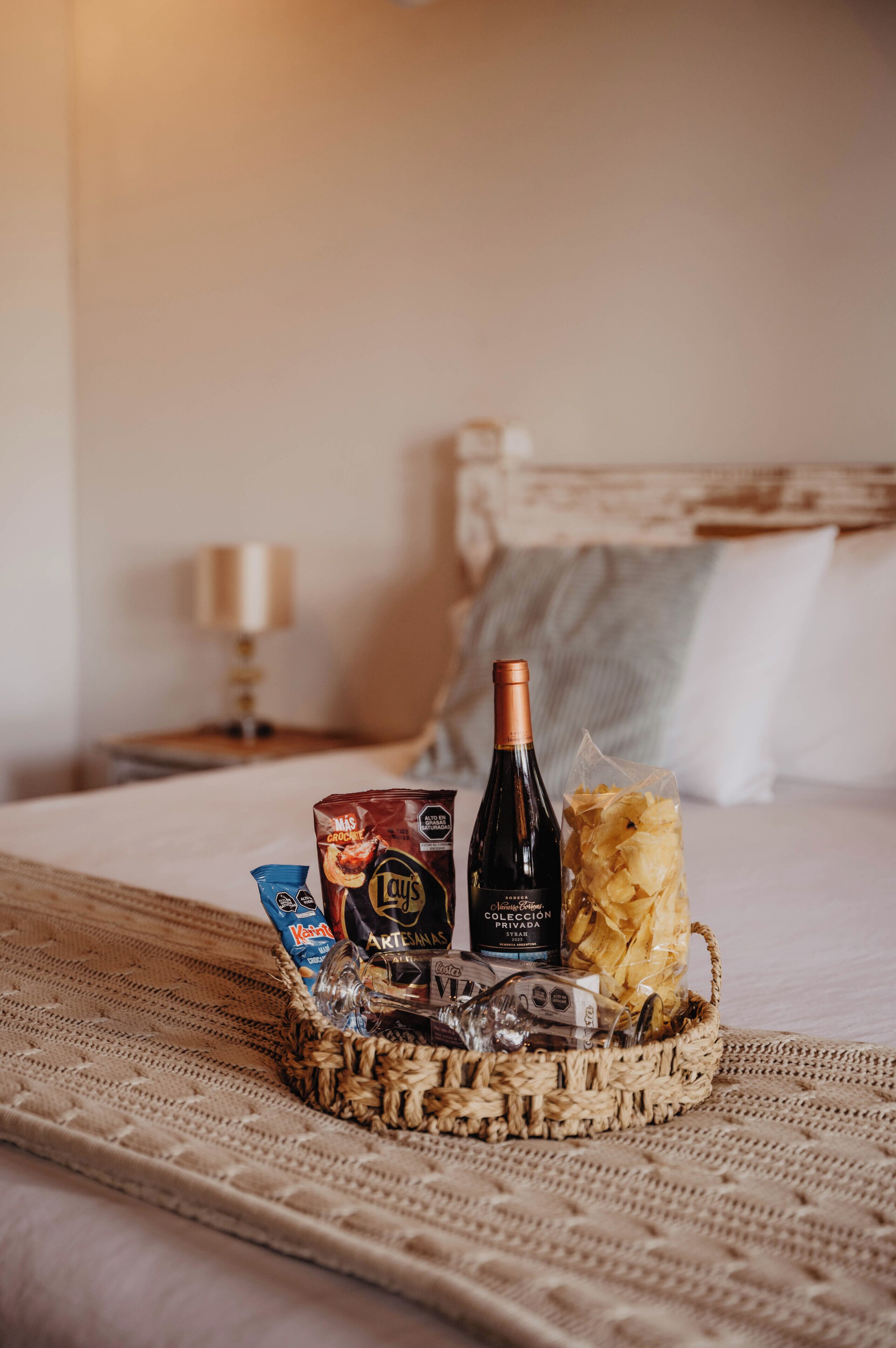 En seng med en kurv der indeholder snacks, en flaske vin og et glas.
