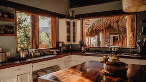 A kitchen with wooden countertops, white cabinets, and a large window overlooking a tropical garden. - VILLA DEL SOL  (Máncora)