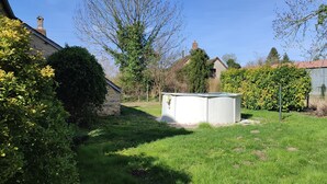 A garden with a white shed, a stone wall, and a variety of trees and shrubs.