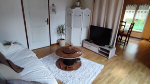 A living room with a sofa, a coffee table, a television, and a dining area with chairs.