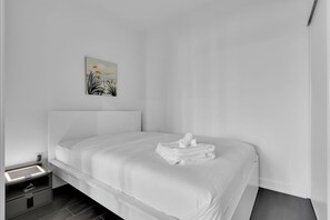 A modern hotel room with a neatly made bed, a bedside table with a lamp, and a painting on the wall. - Modern suite steps to port credit Go (Mississauga)