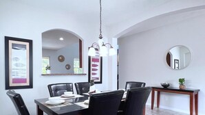 A dining area with a rectangular table, black chairs, a hanging light fixture, and a round mirror on the wall. - Luxurious 6bd Pool Haven Refreshing And Chic-4464n 6 Bedroom Home by RedAwning (Kissimmee)