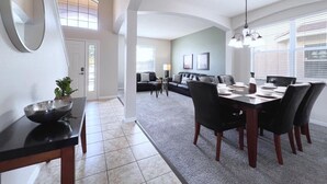 A modern living room with a curved ceiling, a dining area with a black table and chairs, and a large mirror on the wall. - Luxurious 6bd Pool Haven Refreshing And Chic-4464n 6 Bedroom Home by RedAwning (Kissimmee)