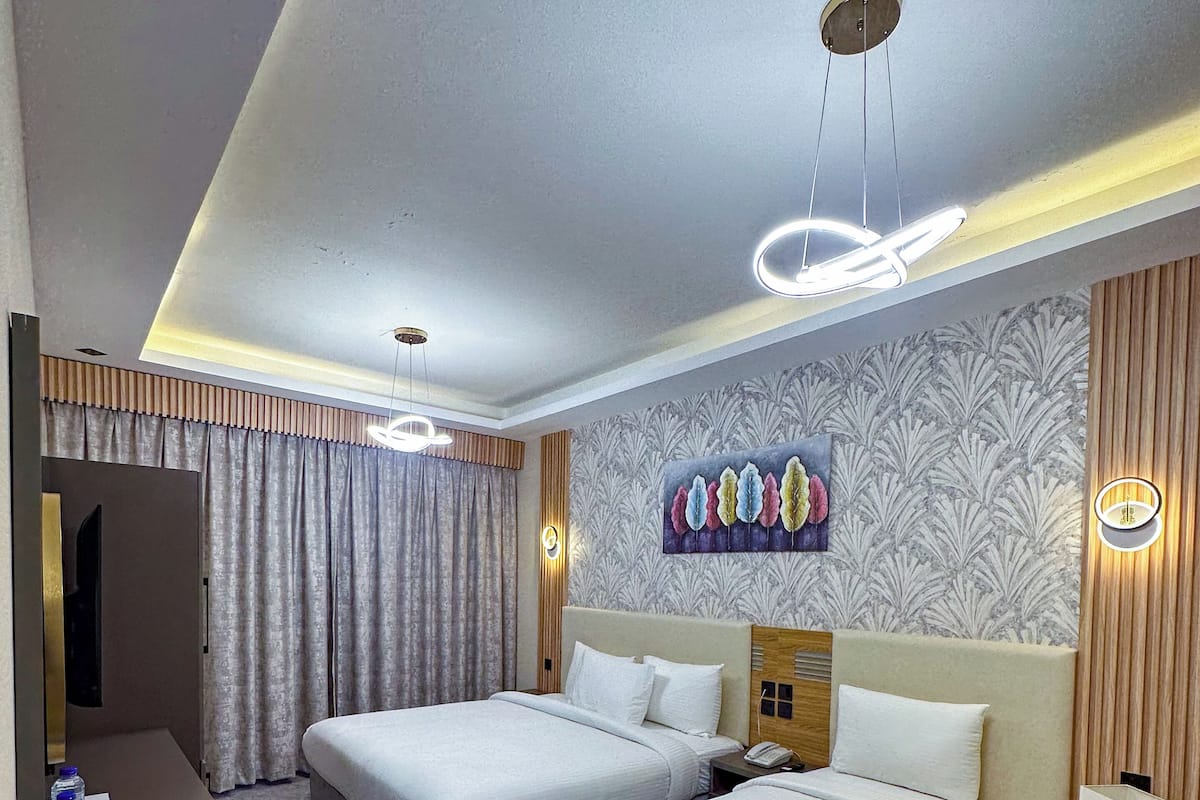 A hotel room with two beds, a desk, a chair, a mirror, and a painting on the wall.