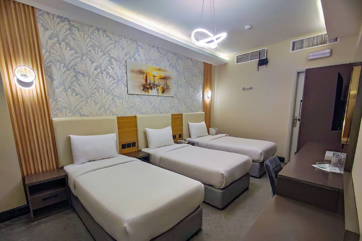 A hotel room with three single beds, a small desk, a mirror, and a painting on the wall.