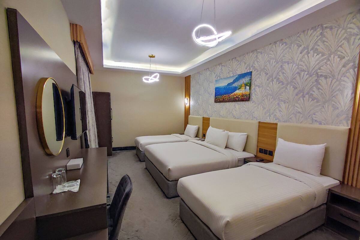 A hotel room with two beds, a desk with a mirror, a chair, and a painting on the wall.