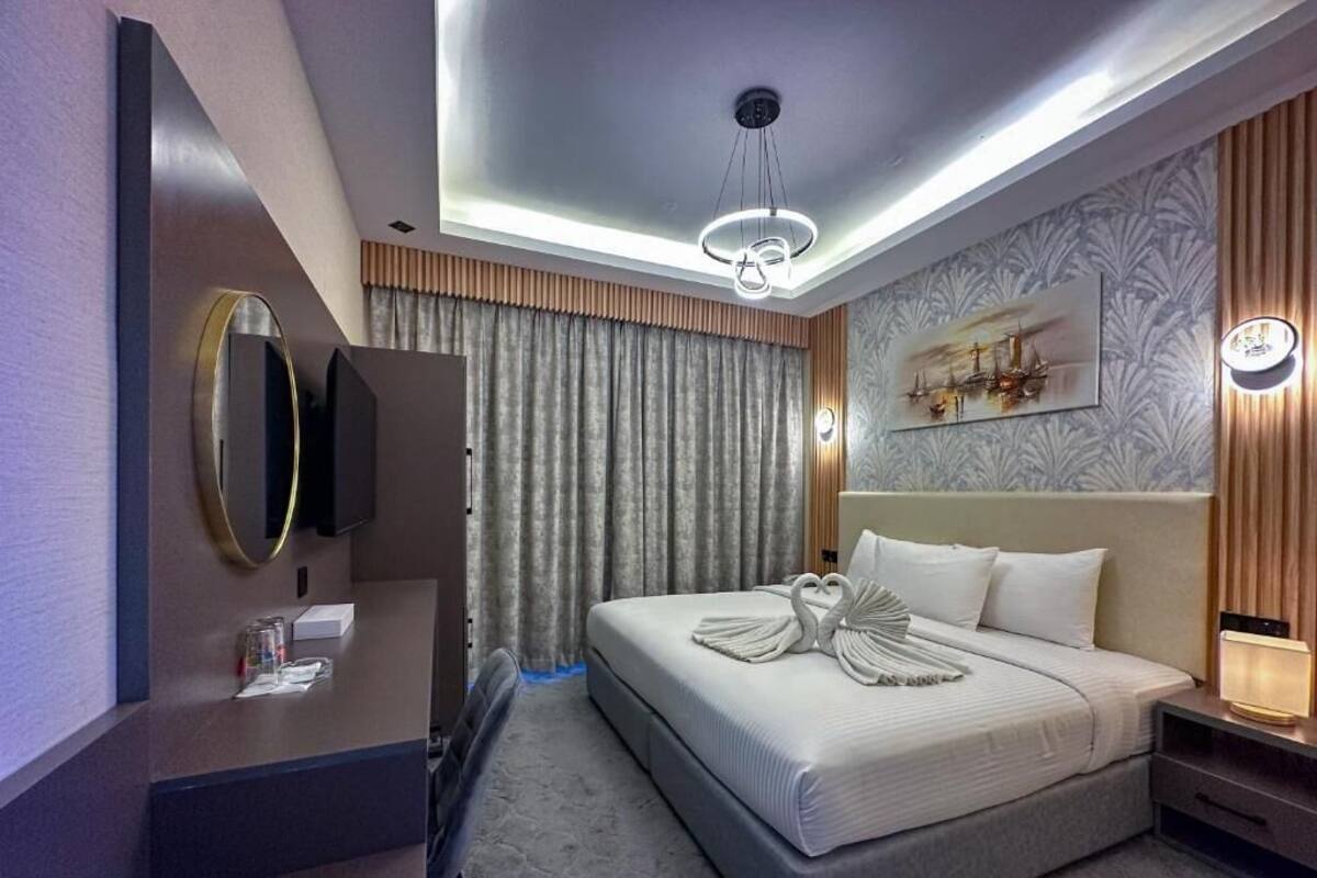 A modern hotel room with a large bed, a desk with a mirror, a flat-screen TV, and a wall-mounted artwork.