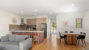 Una cocina moderna con una isla central, un comedor con mesa y sillas de madera, y un sofá gris en la sala.