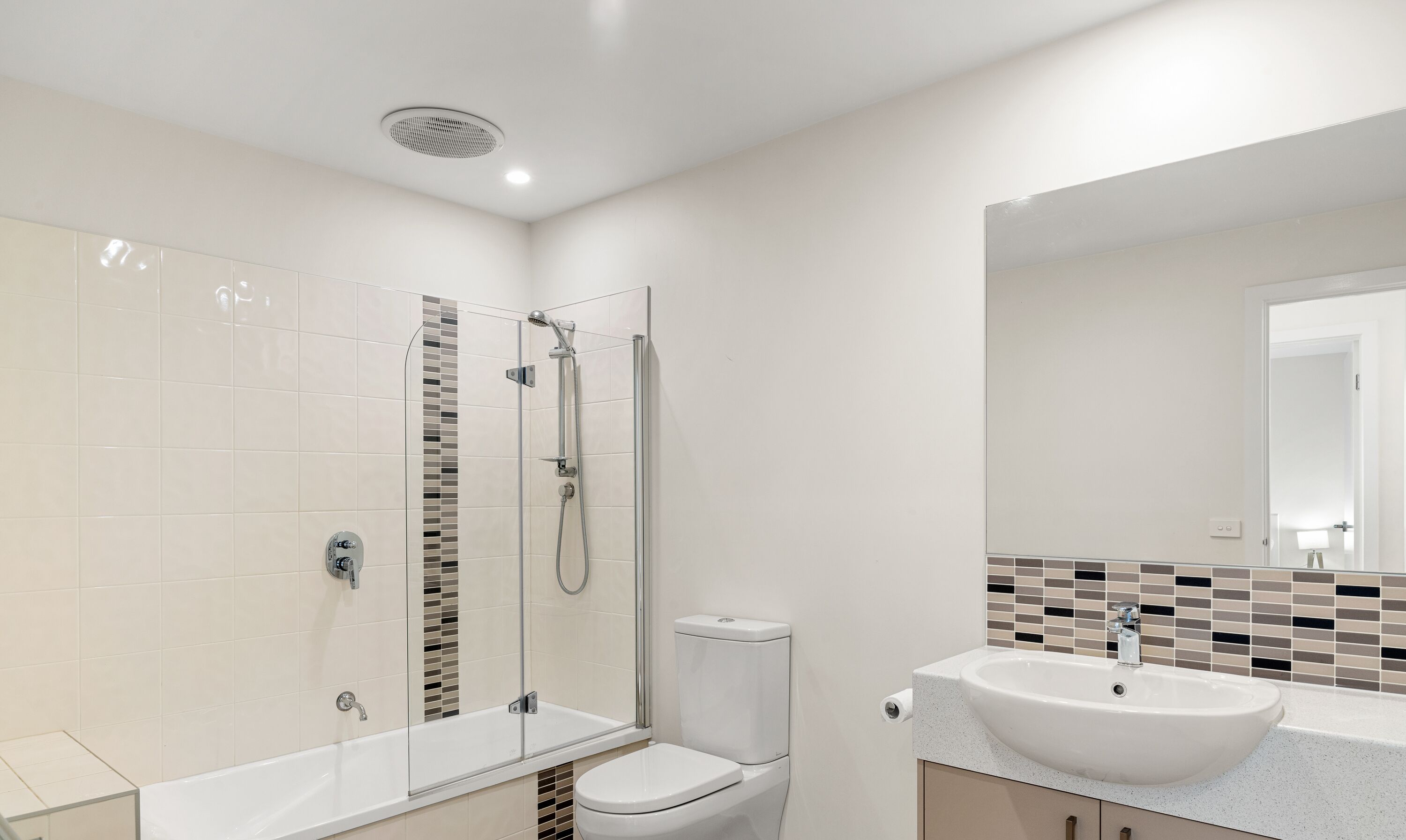 Une salle de bain moderne avec une douche à parois de verre, des toilettes blanches et un lavabo avec un miroir au-dessus.
