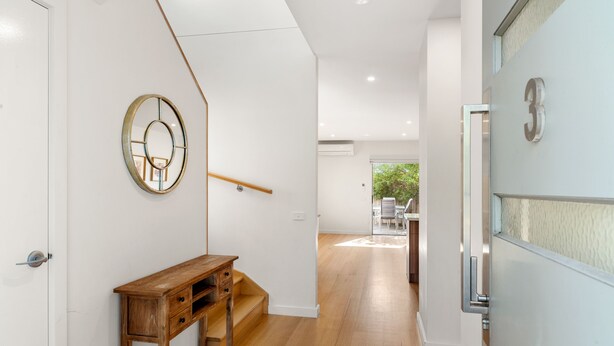 Un interior moderno con un banco de madera, un espejo fijado a la pared y una escalera que conduce a otra habitación.